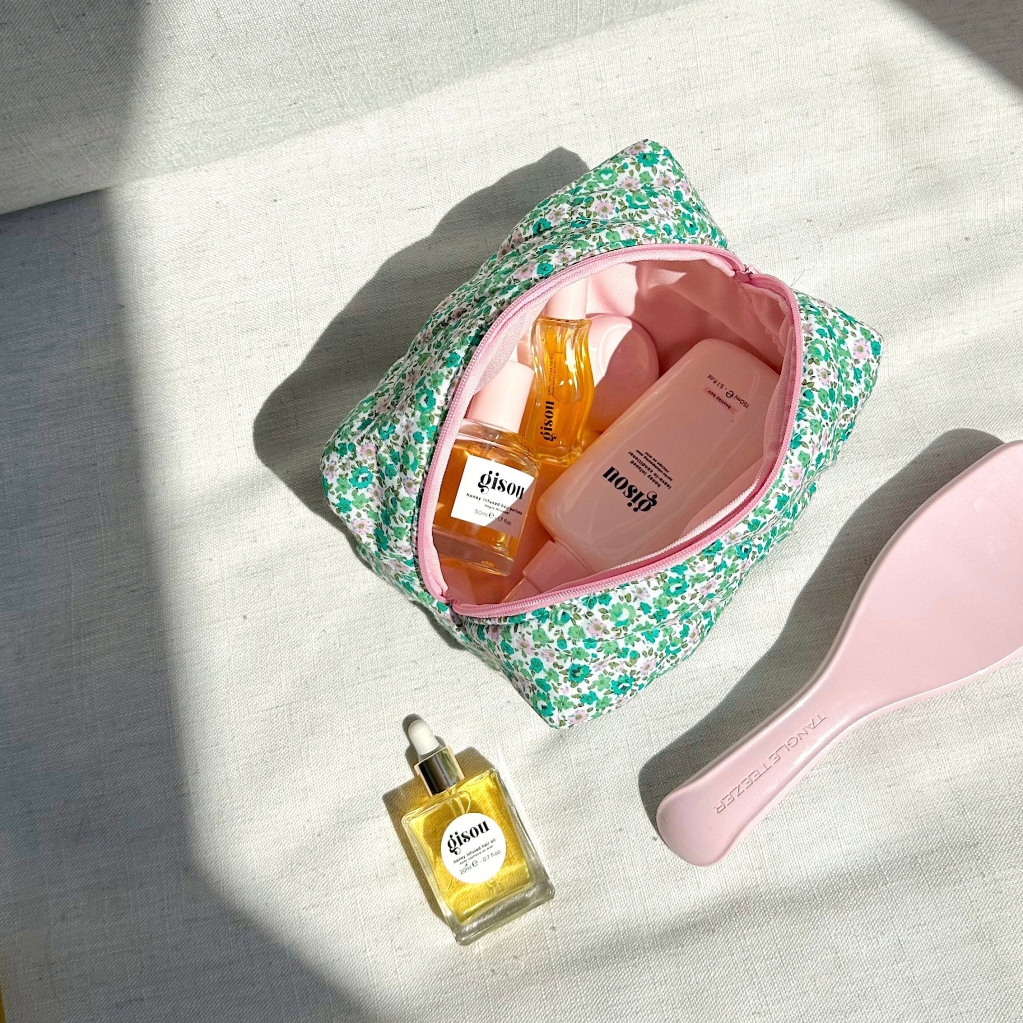 Green and pink floral cosmetic pouch open with pink lining, showing skincare bottles inside