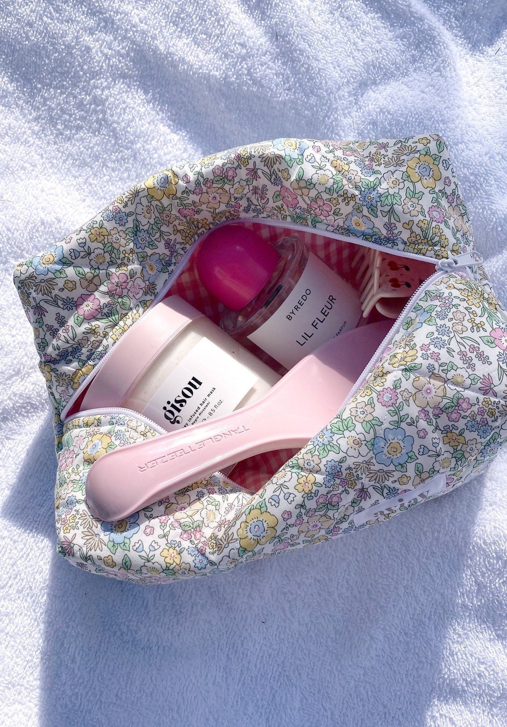 Pastel floral makeup bag open, showing pink gingham lining and toiletries inside