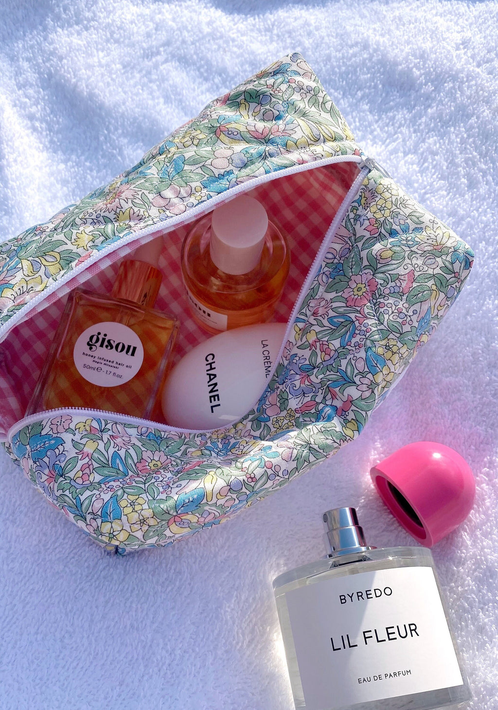 Floral zip pouch with multicolor flower print and pink gingham lining, open with bottles