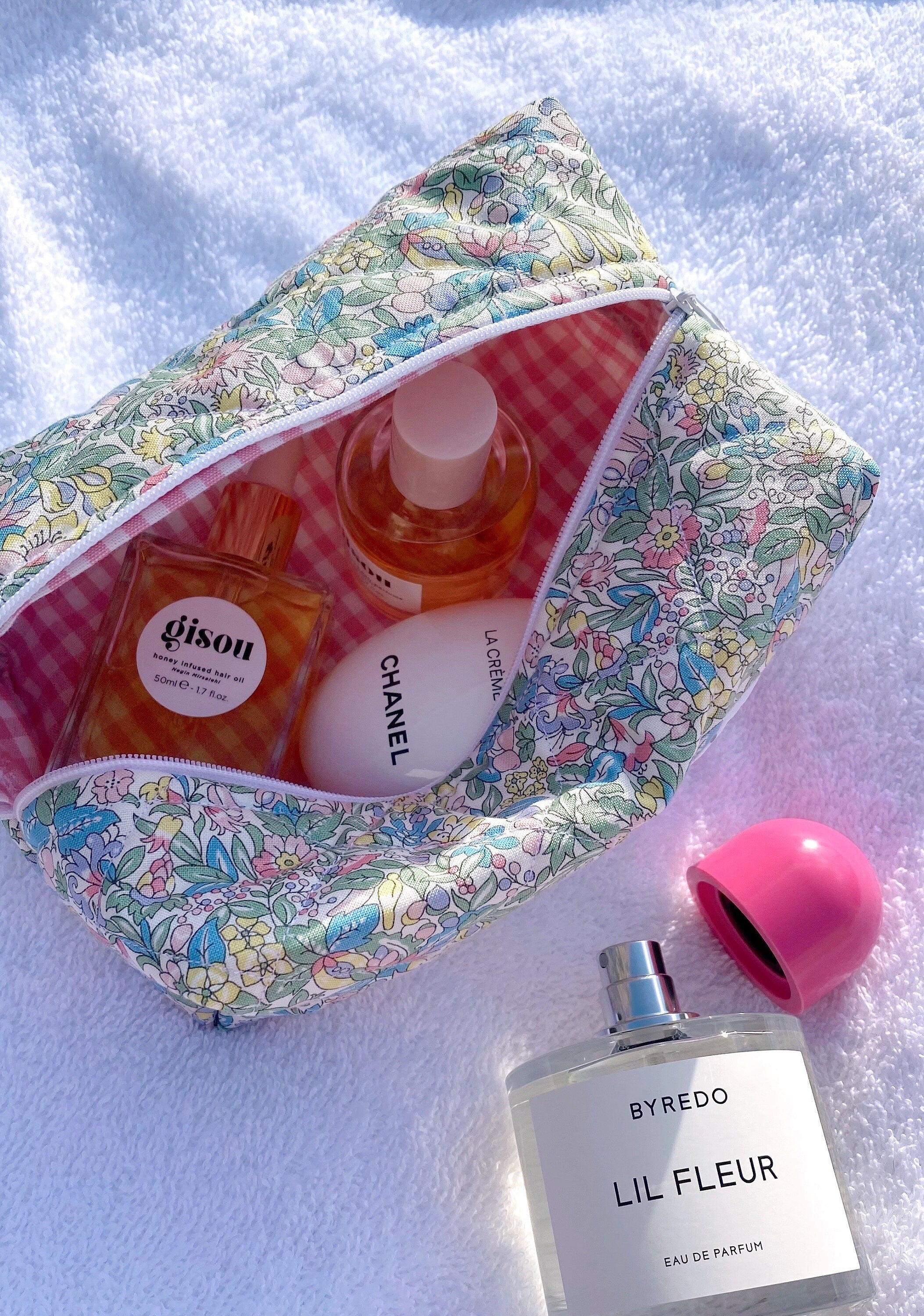 Floral zip pouch with multicolor flower print and pink gingham lining, open with bottles