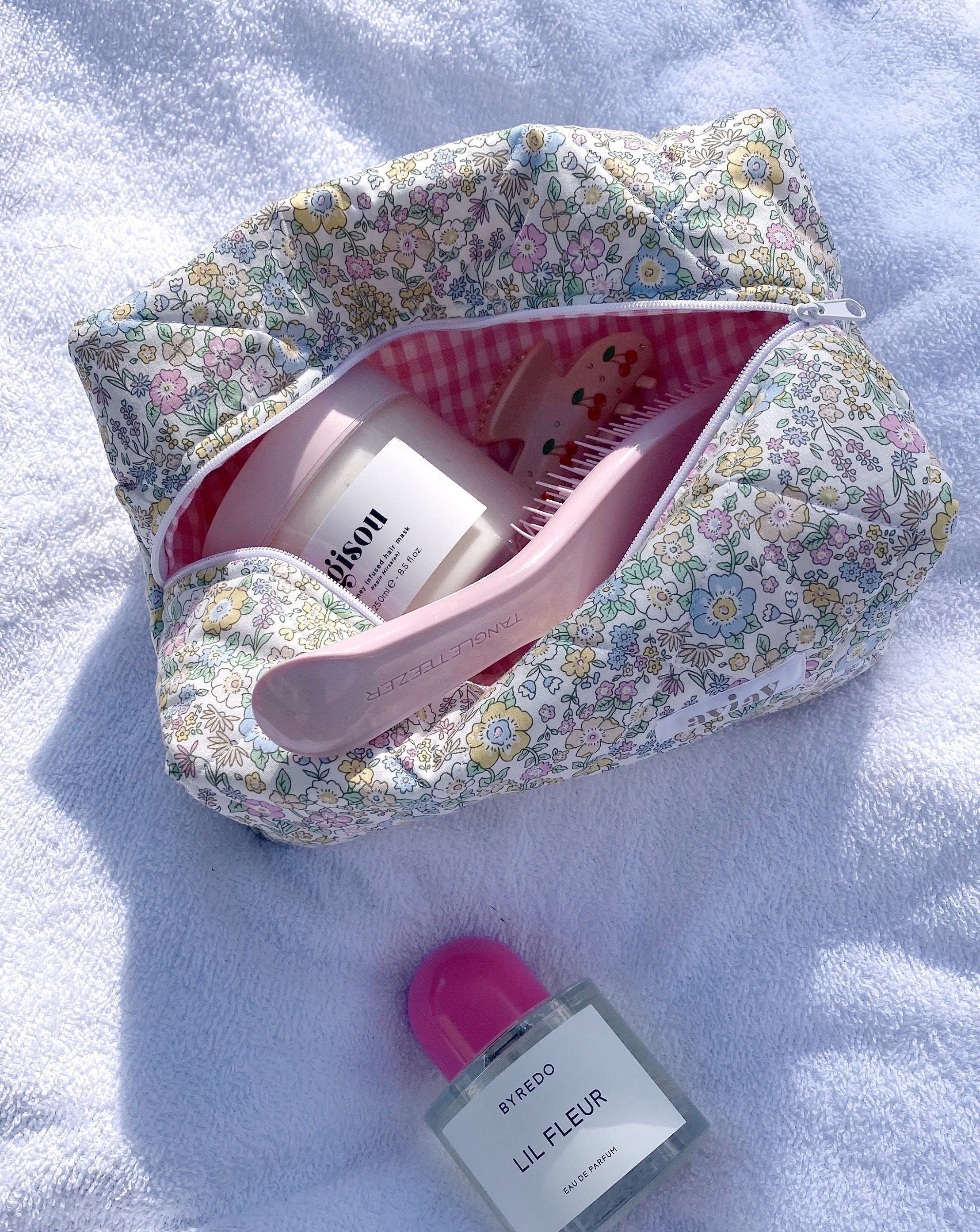 Pastel floral makeup bag open with pink gingham lining and cylindrical bottles inside