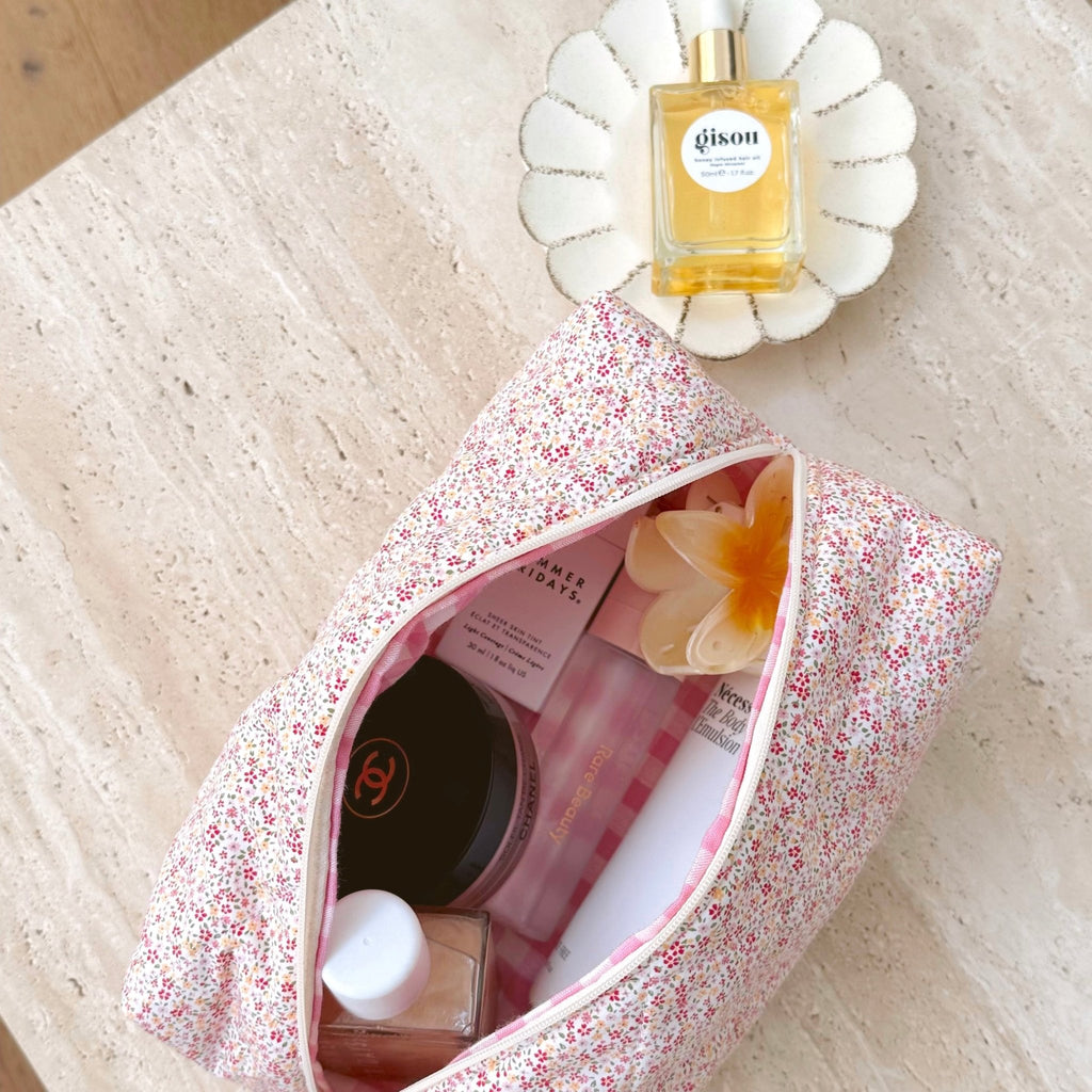 Pink floral zip-top cosmetic pouch, open with items inside