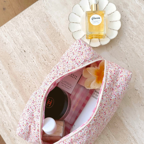 Pink floral zip-top cosmetic pouch, open with items inside