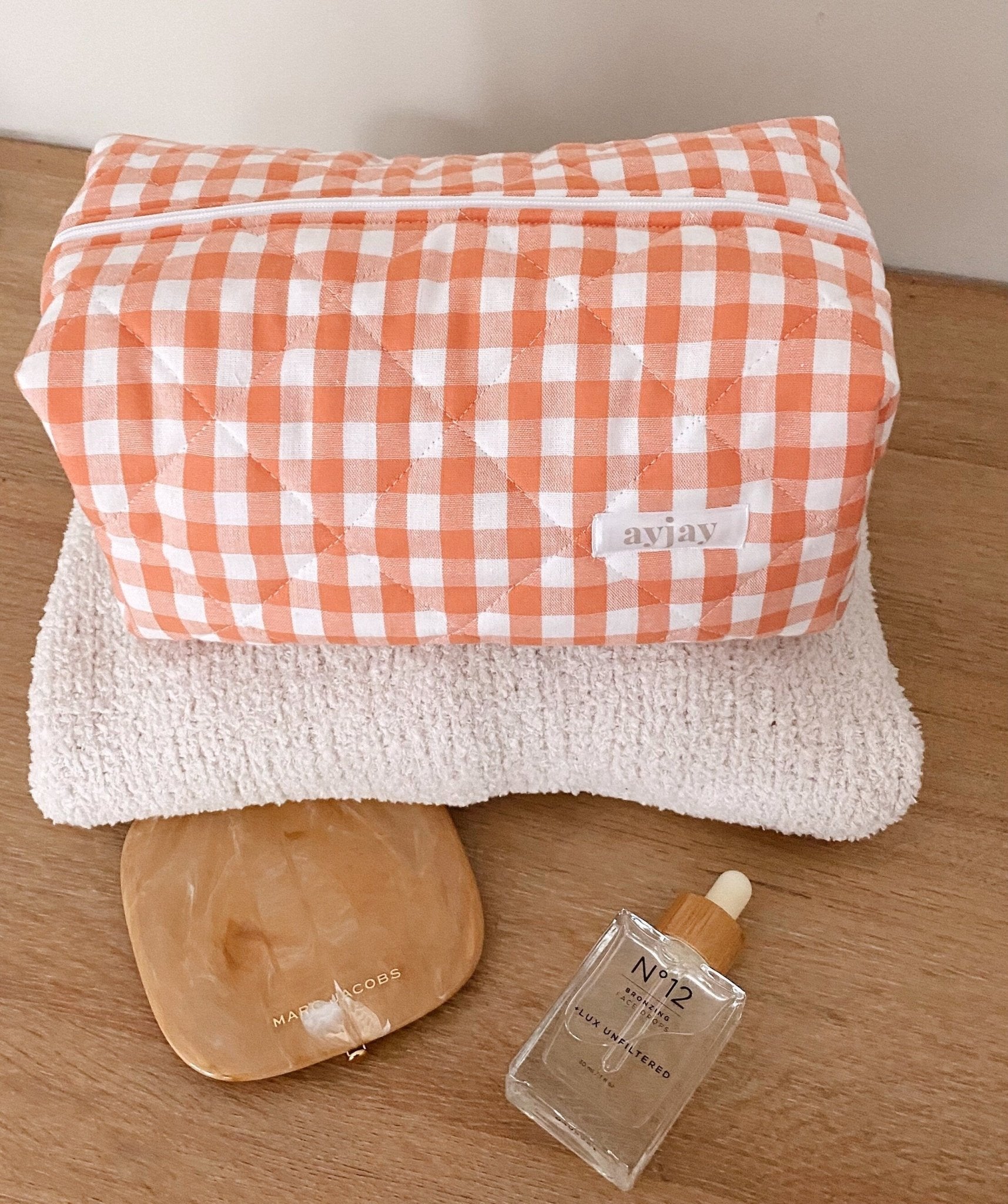 Orange gingham zip-top cosmetic pouch with white trim and stitched logo panel