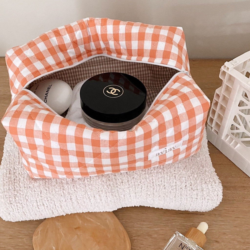 Orange gingham cosmetic pouch open, showing gingham-lined interior and top zipper