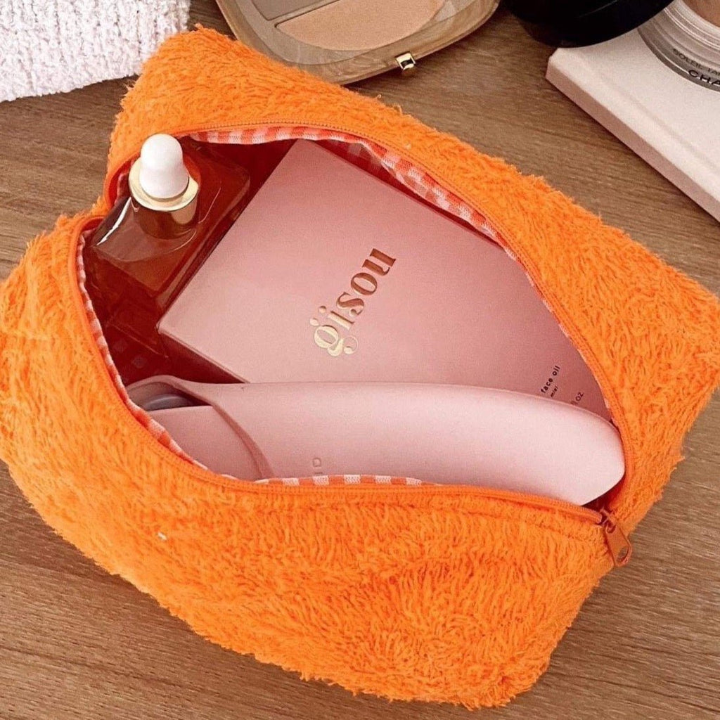 Orange teddy pouch open with items inside; orange zipper edge and plaid inner lining