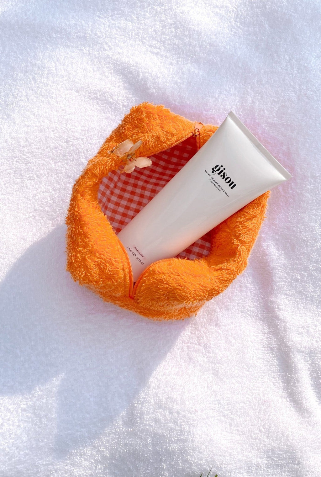 Orange fluffy teddy pouch with zip top open, plaid interior holding white tube