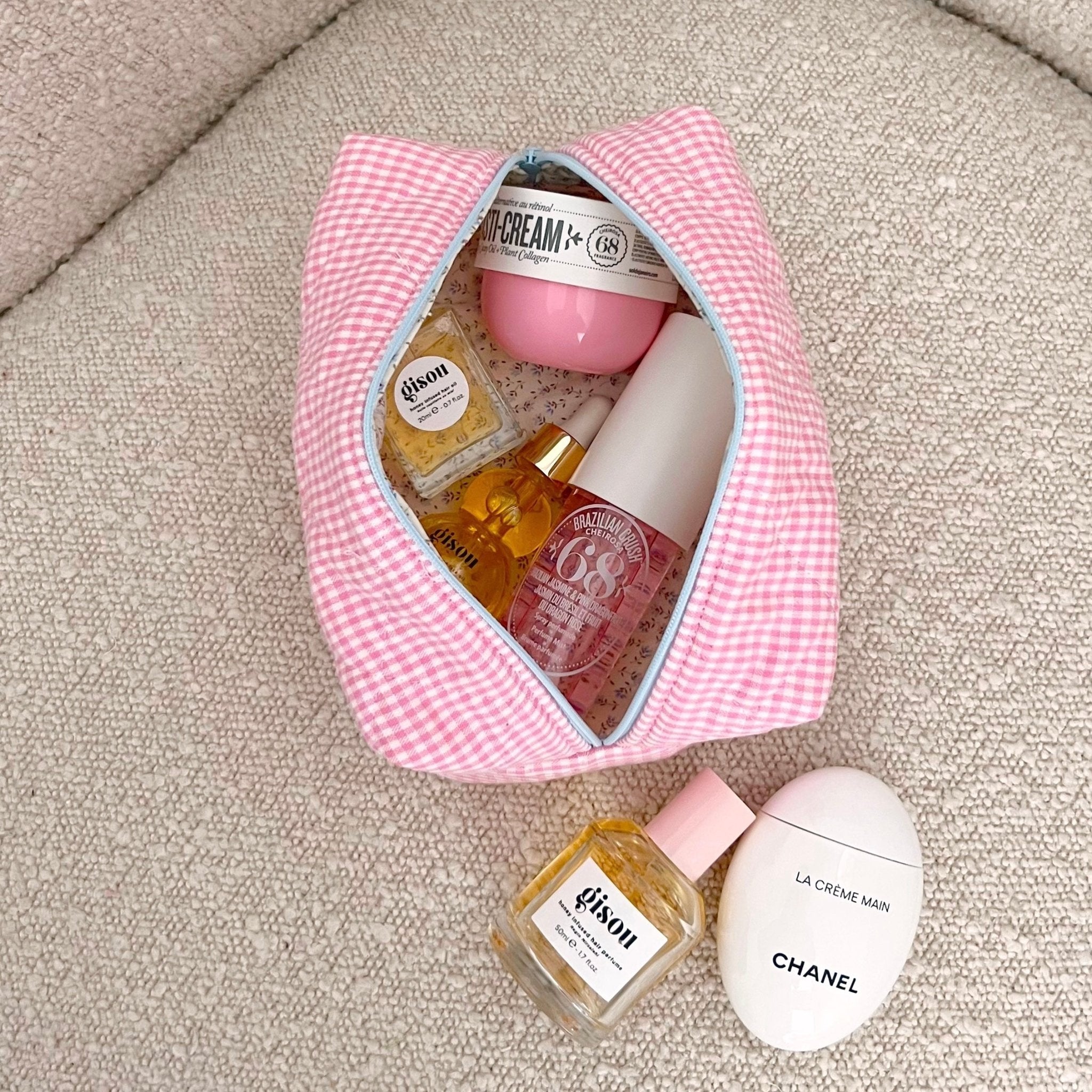 Open pink gingham cosmetic pouch with blue edging, packed with skincare bottles