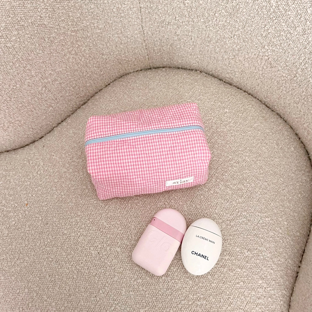 Pink gingham zip pouch with blue trim and small rounded bottles beside it