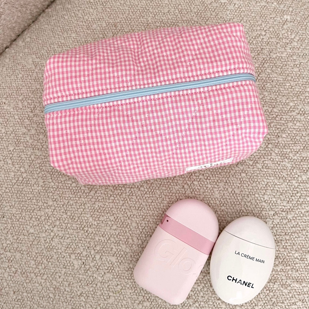 Pink gingham zip pouch with light blue piping, shown folded on beige fabric