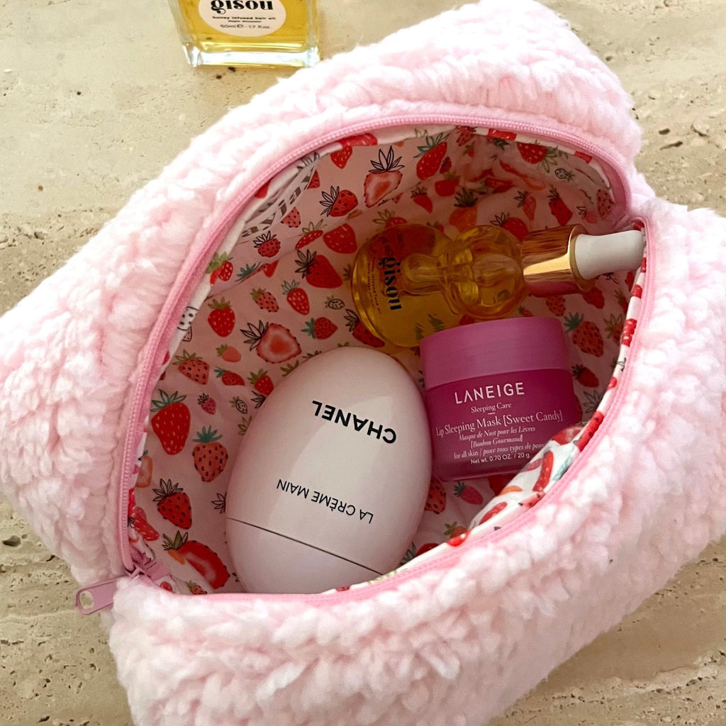 Pink teddy makeup bag with strawberry-pattern lining, zippered opening, holds face cream.
