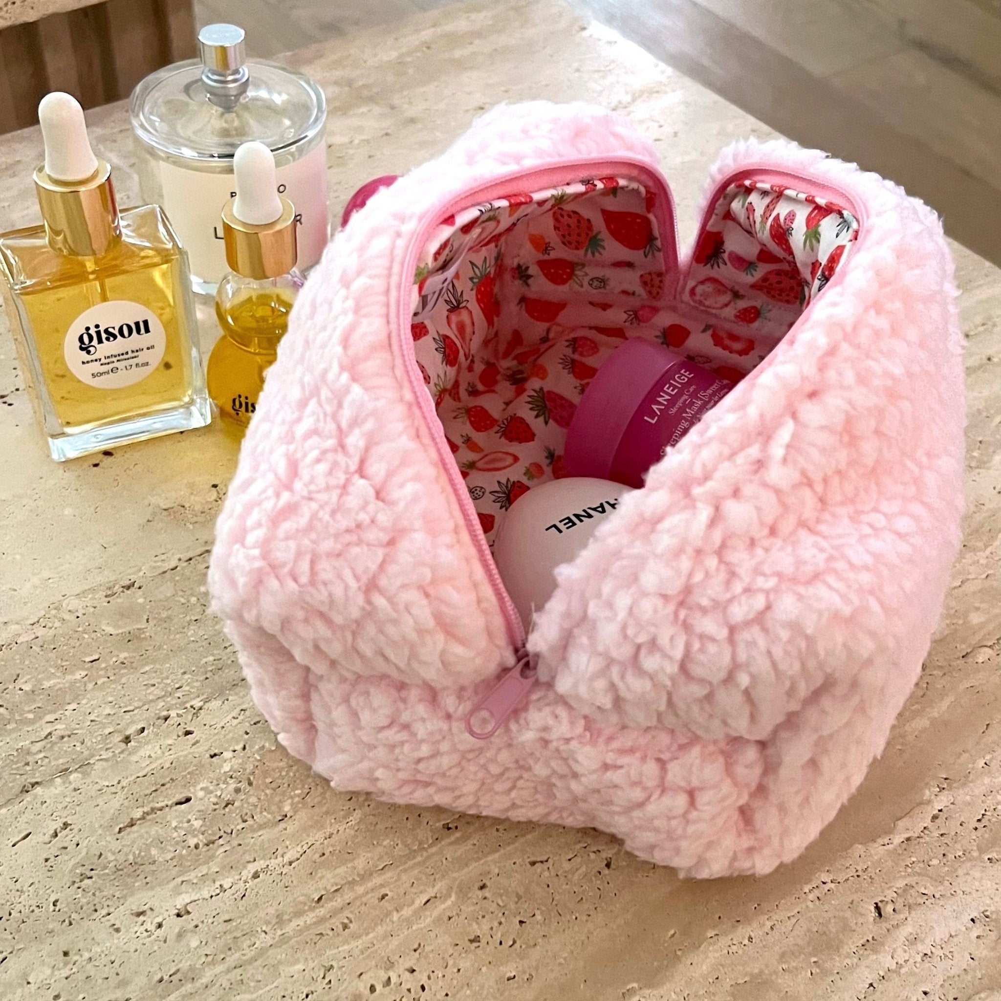 Pink teddy cosmetic pouch, zip top open with strawberry-pattern lining and products.
