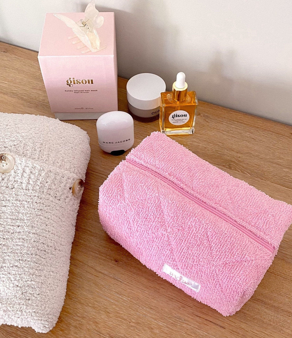Pink terrycloth zip pouch on wood, front label and zipper track visible.