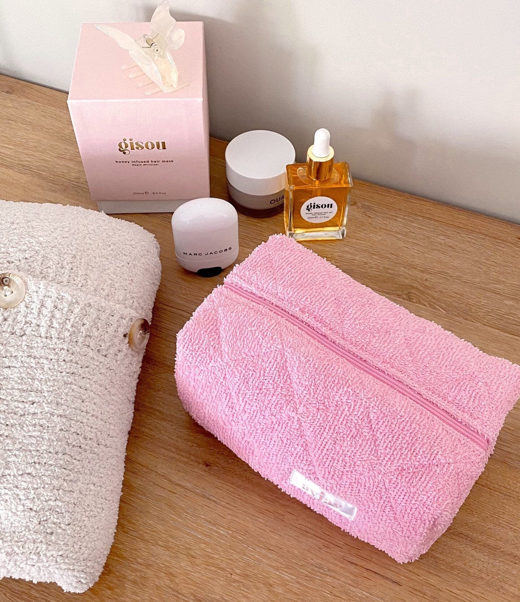 Pink terrycloth zip pouch on wood, front label and zipper track visible.