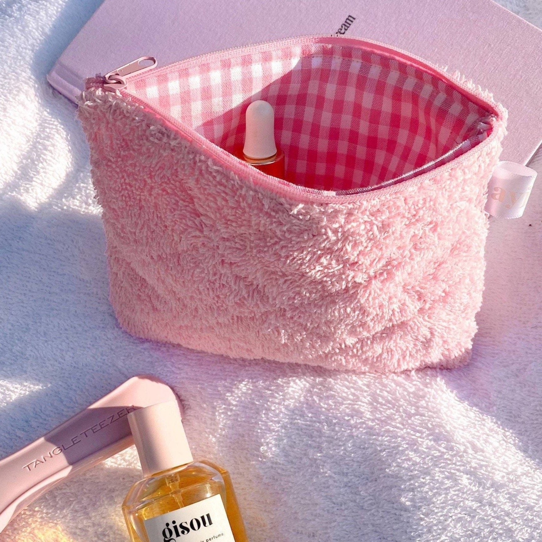 Pink terrycloth pouch with red check lining, zipper top and inner fabric visible.