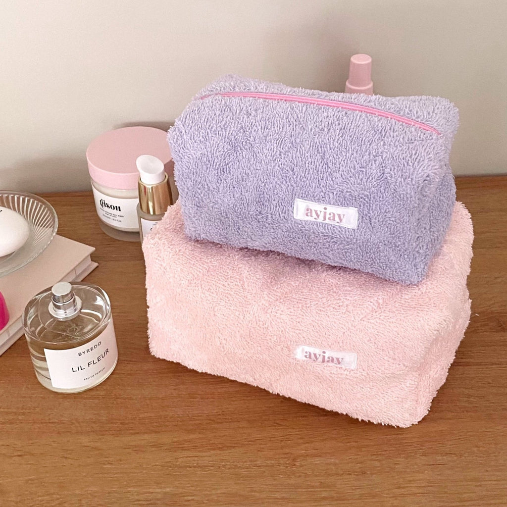 Lavender and pink terrycloth zip pouches stacked, each with pink trim and logo label