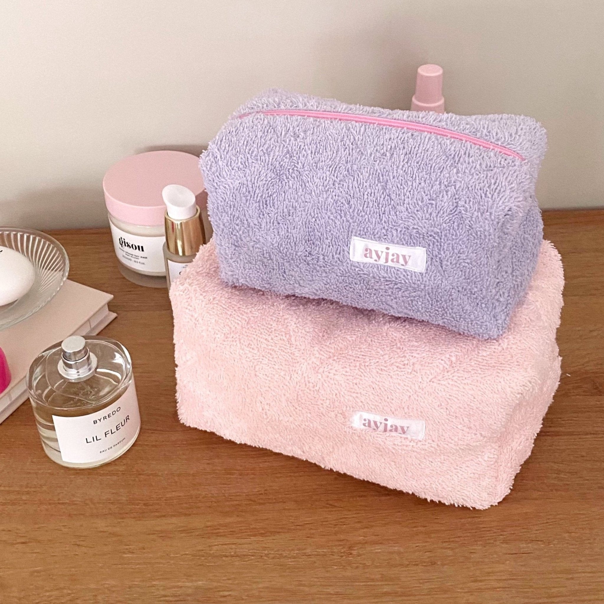 Lavender and pink terrycloth zip pouches stacked, each with pink trim and logo label