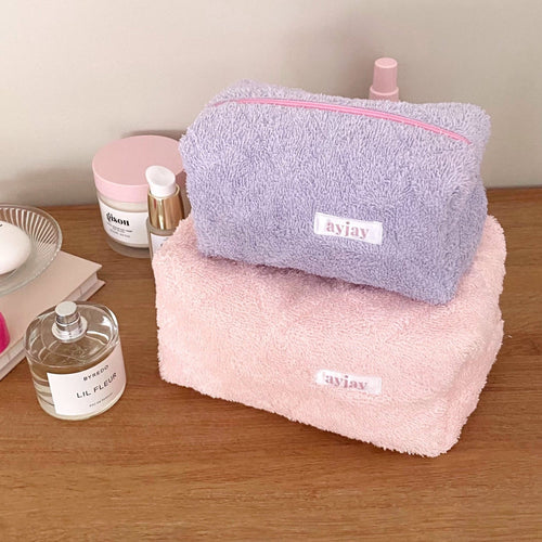 Lavender and pink terrycloth zip pouches stacked, each with pink trim and logo label