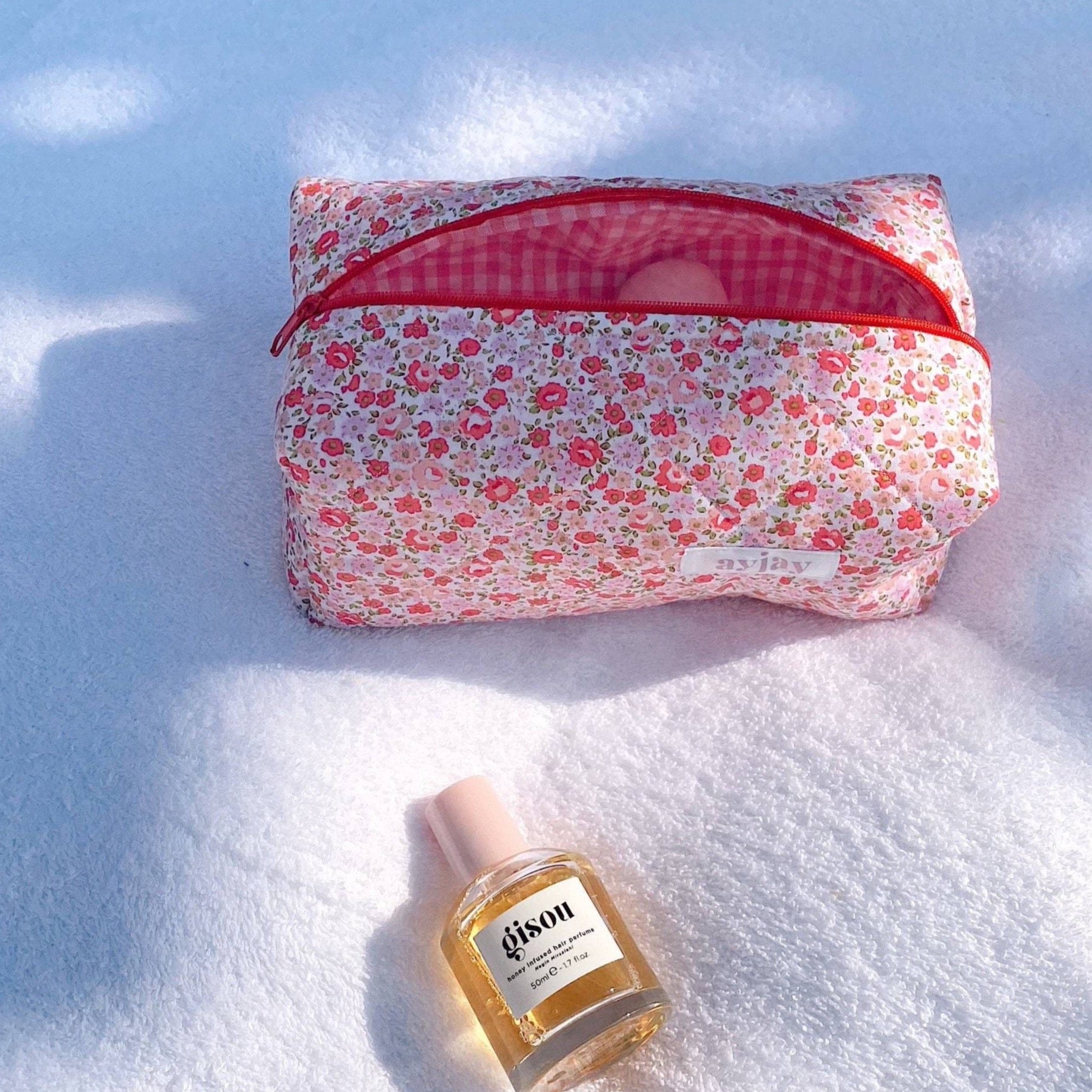 Pink gingham-lined floral pouch with red zipper, closed, rectangular cosmetic bag