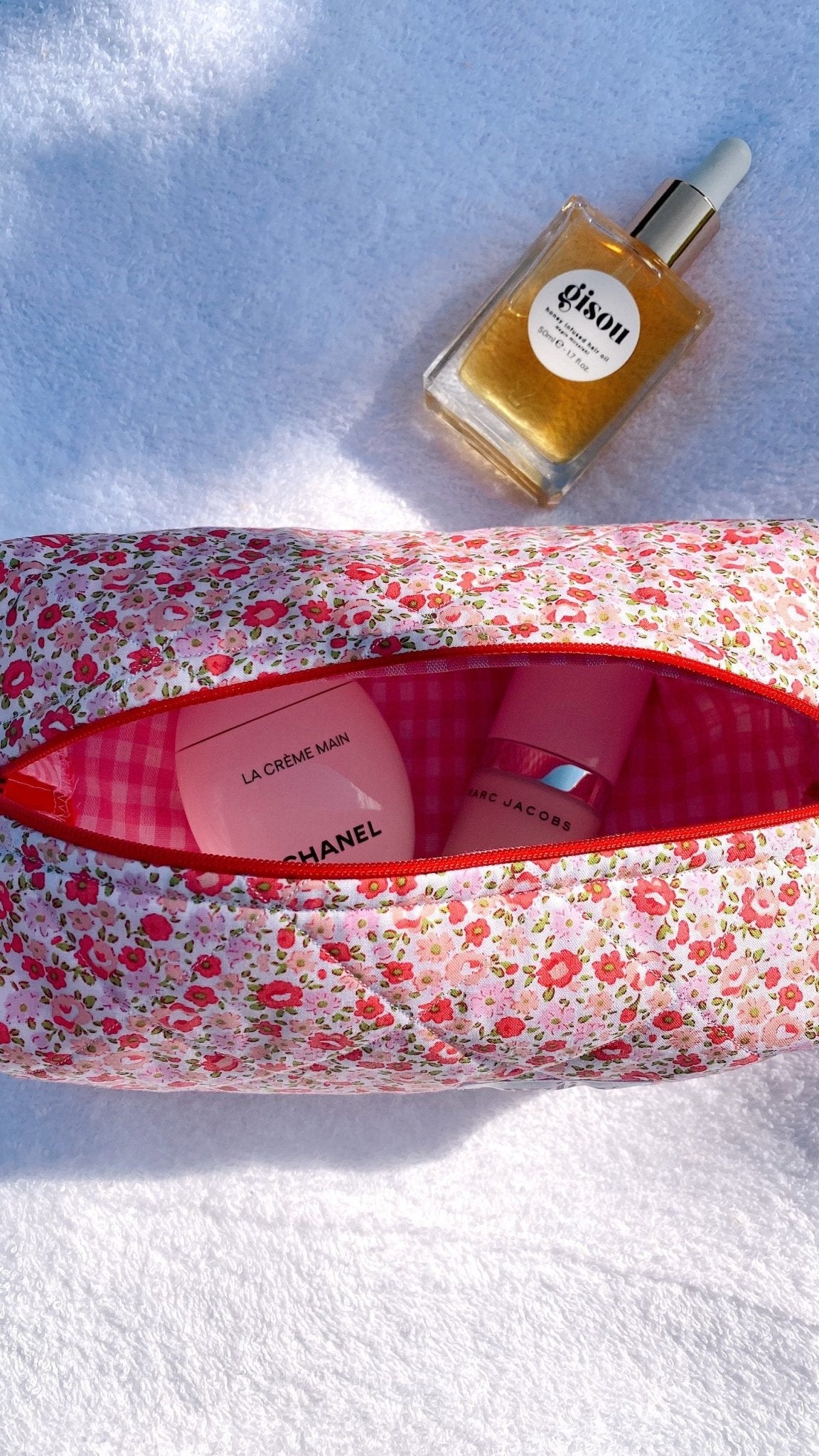 Floral zip pouch with pink gingham lining open, red zipper edge, beside oil bottle