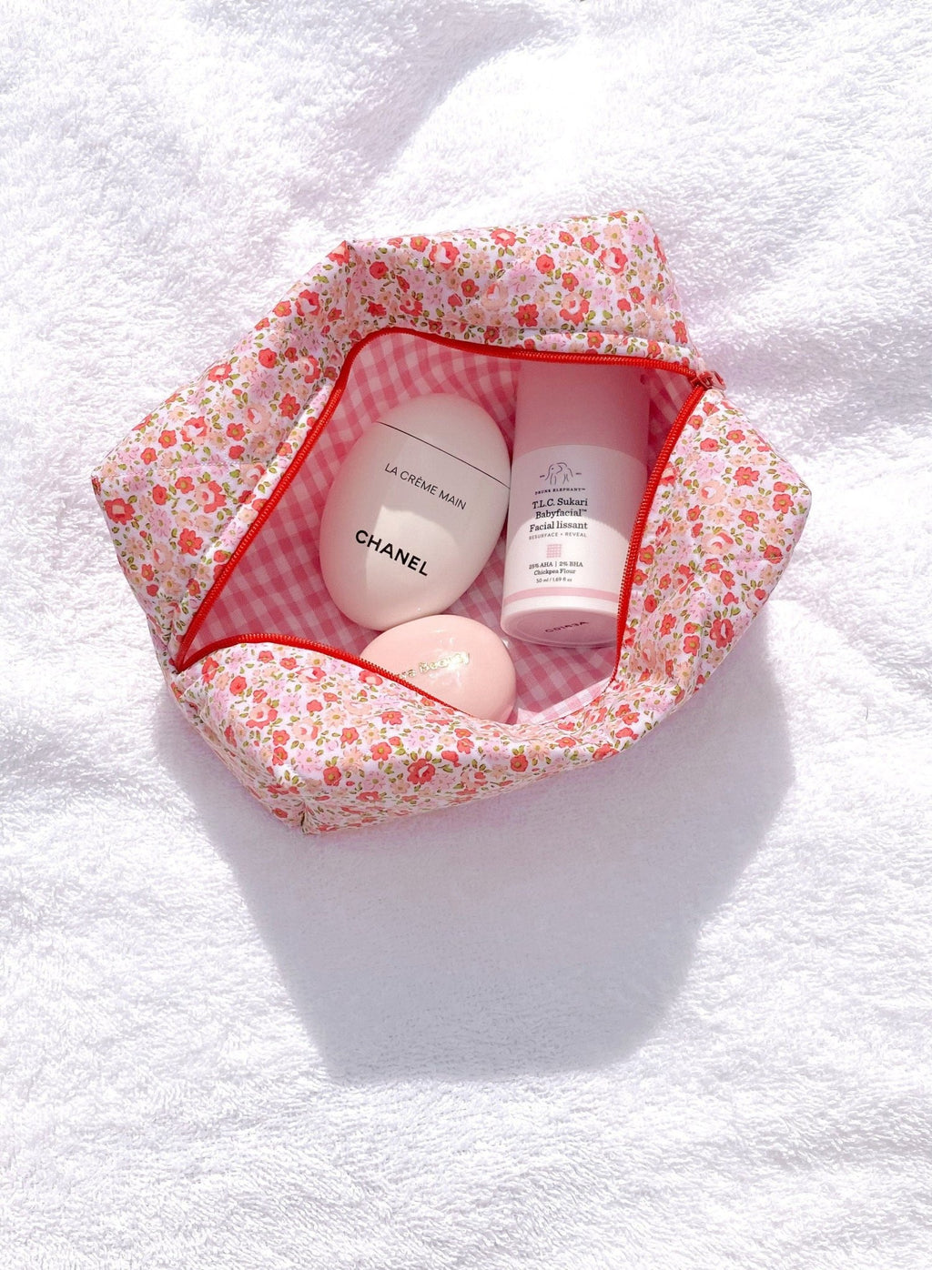 Floral cosmetic pouch open to pink gingham lining, showing cream tubes inside