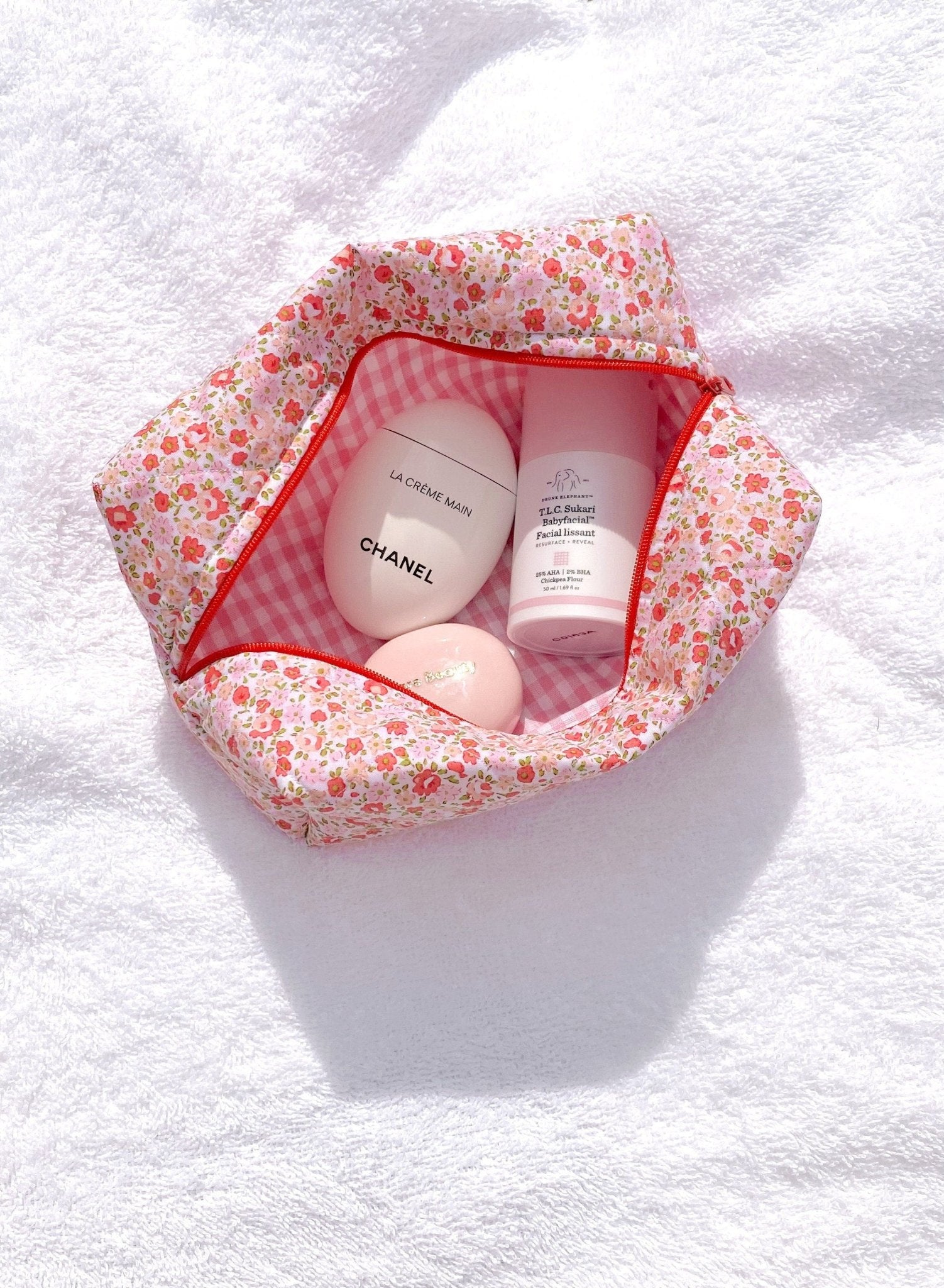 Floral cosmetic pouch open to pink gingham lining, showing cream tubes inside