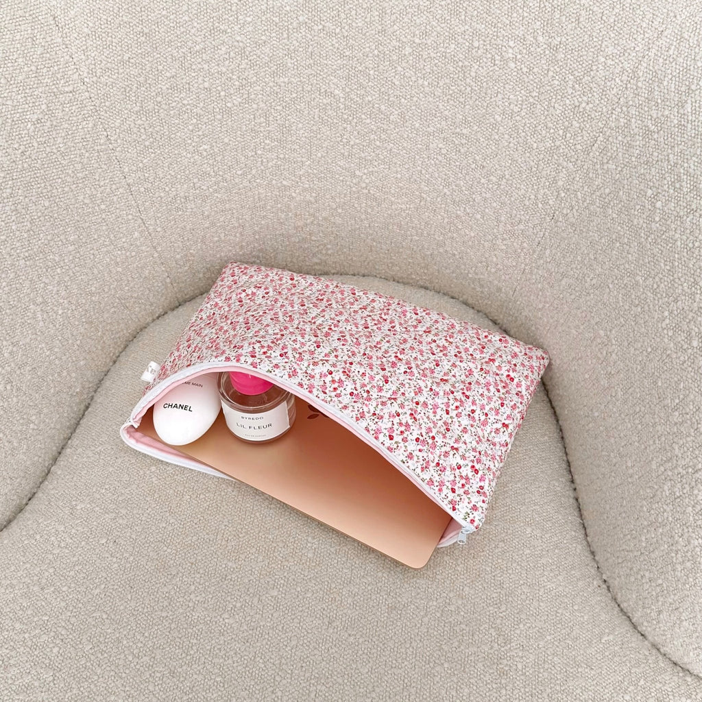Pink floral zip pouch lying open on fabric, showing empty interior lining.