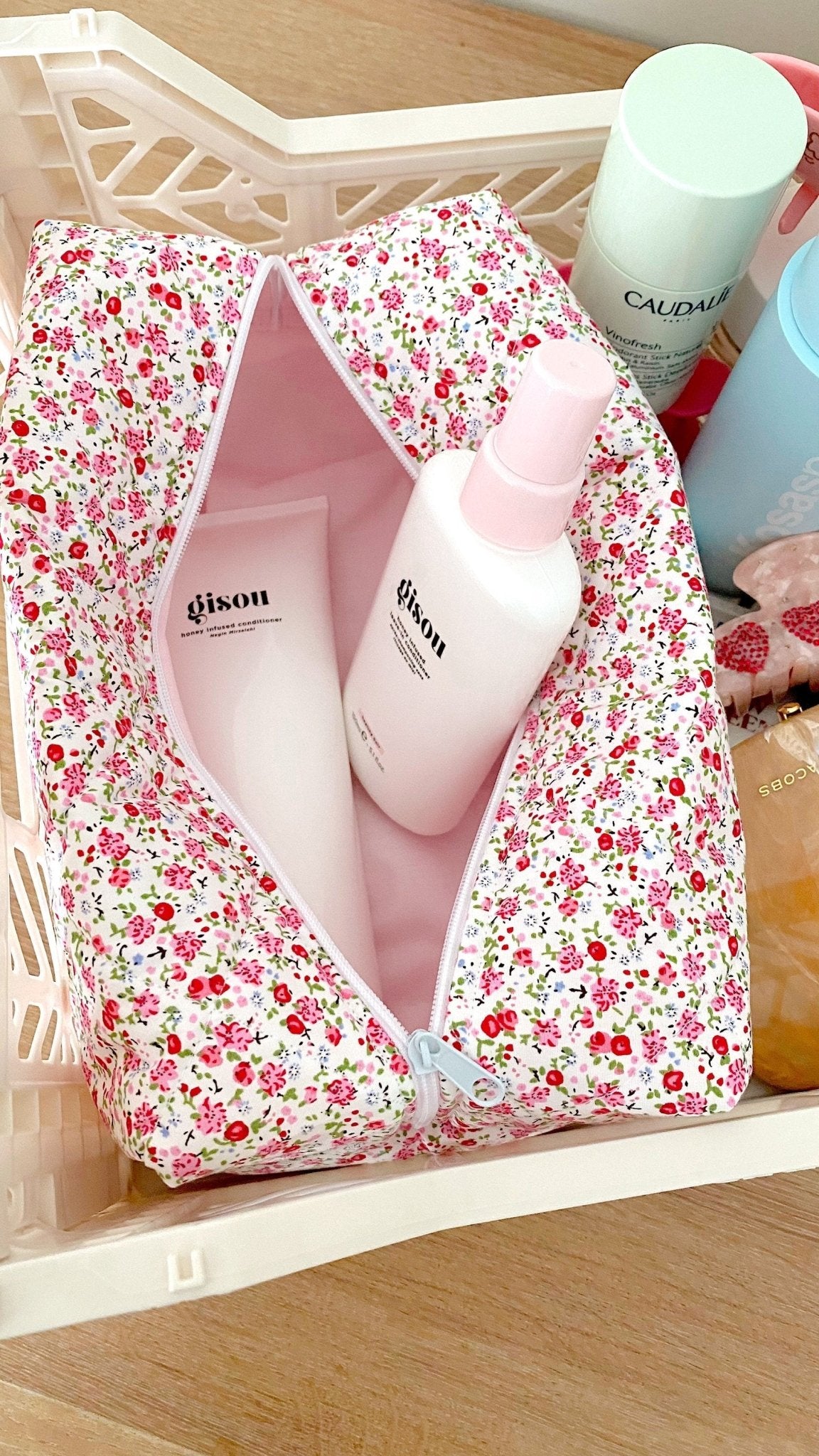 Floral zip pouch on a tray, open front shows pink-lined compartments and bottles.