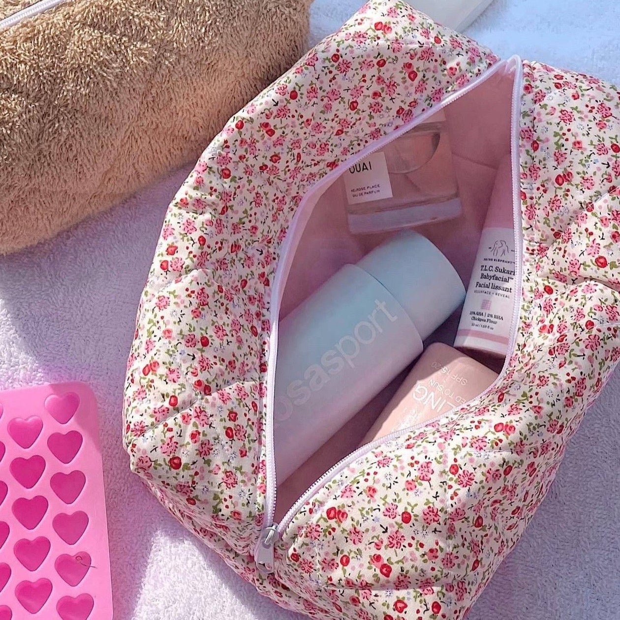 Light pink floral toiletry bag with zip opening and light pink lining, front view.