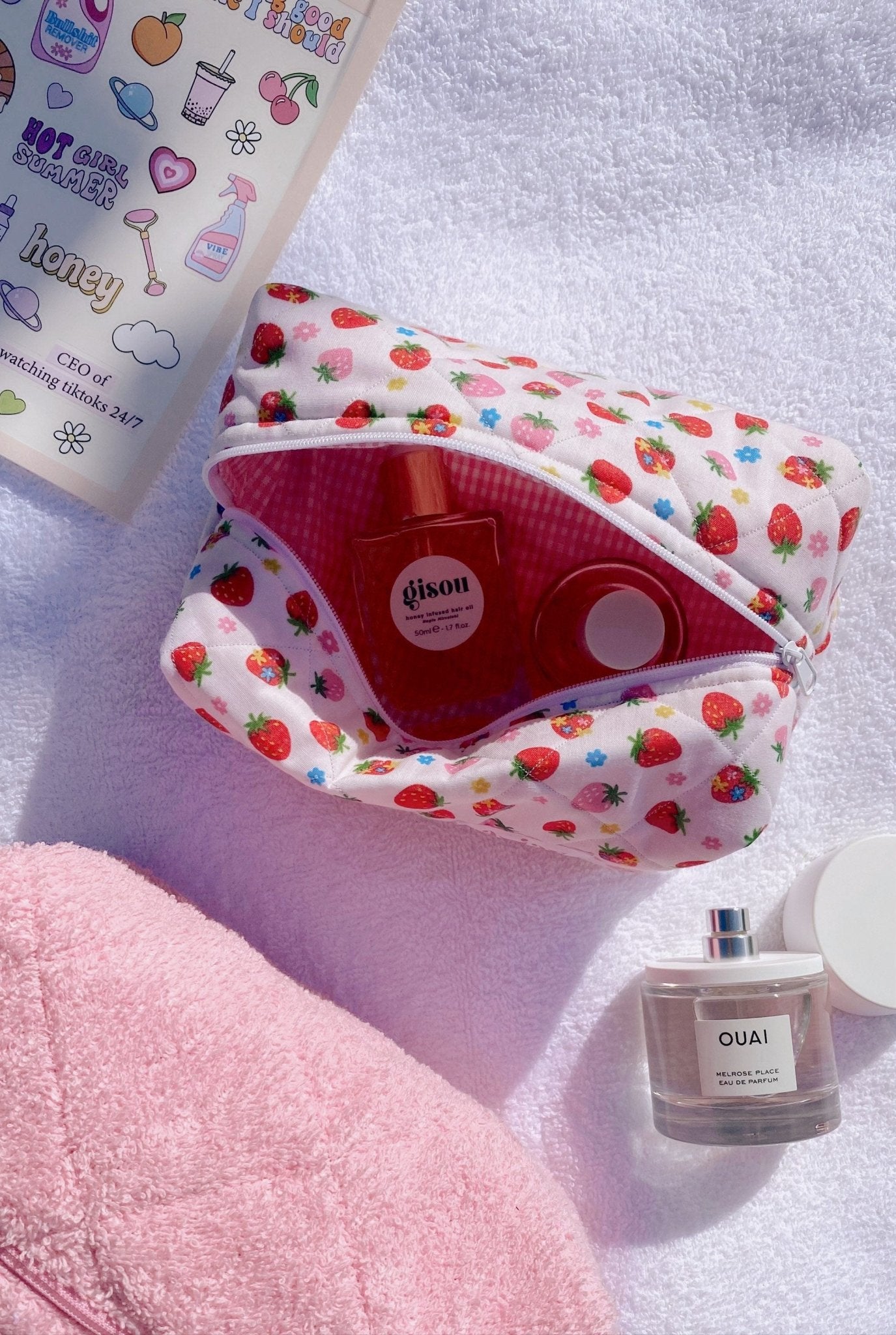 Strawberry floral zip pouch open, red lining and bottles inside; stitched zipper top
