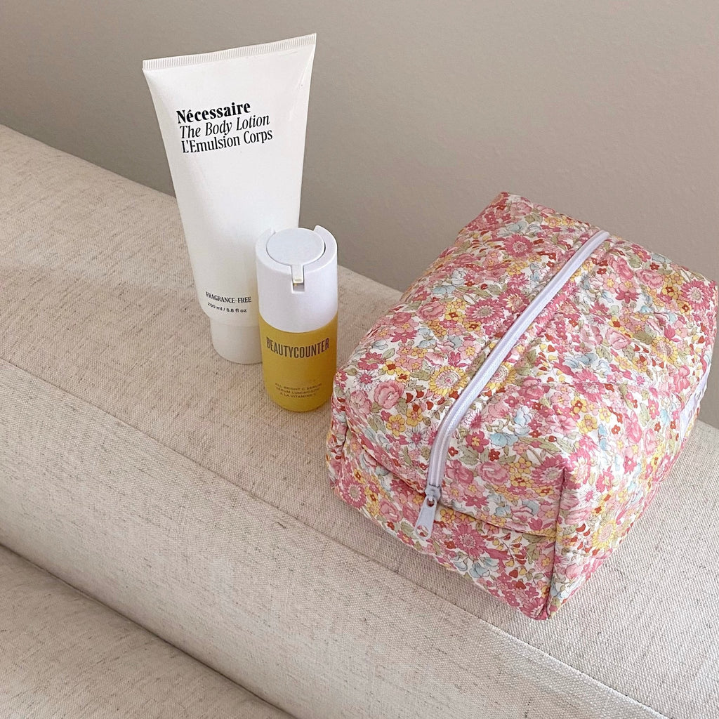 Pink floral cosmetic bag with zipper, compact rectangular shape on sofa