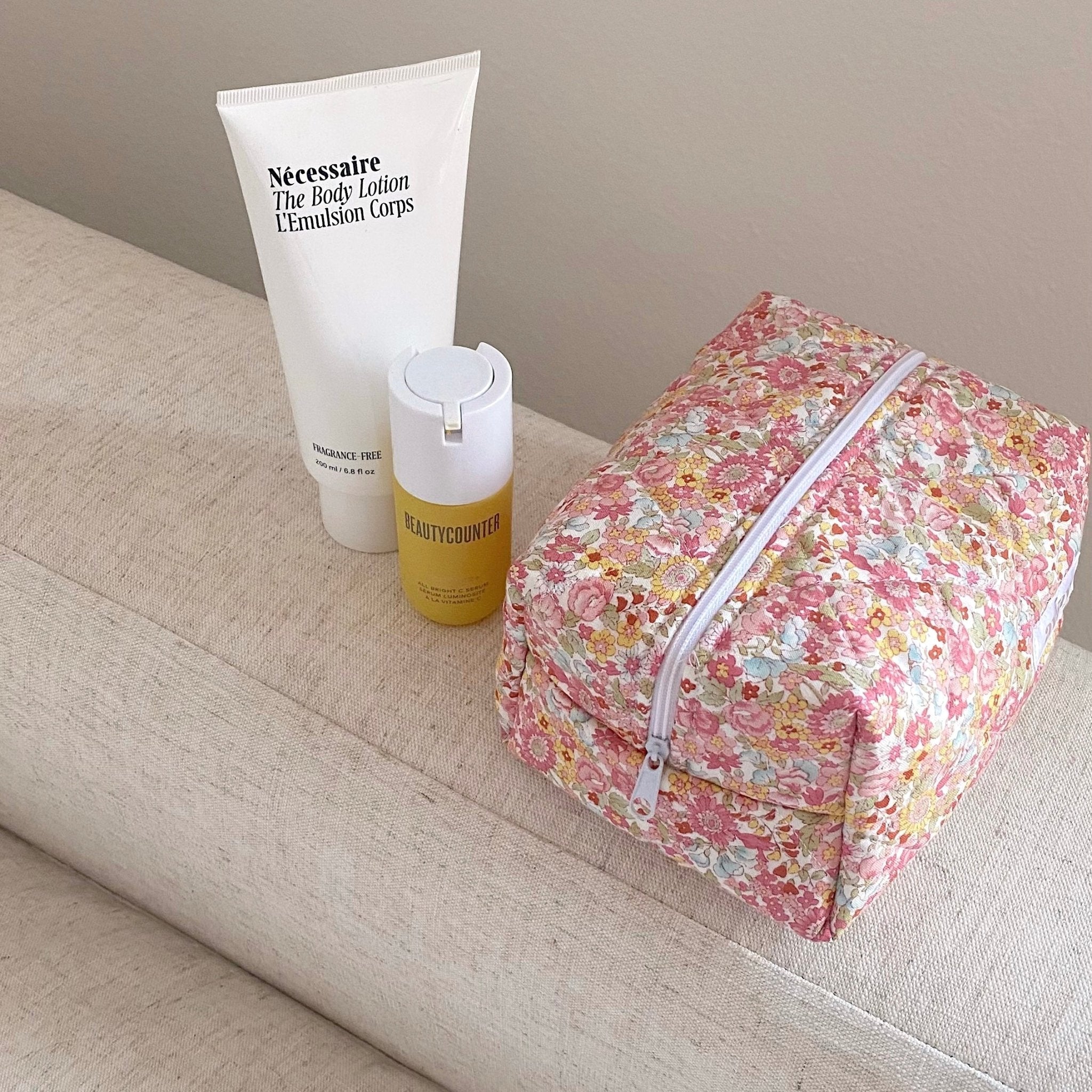 Pink floral cosmetic bag with zipper, compact rectangular shape on sofa