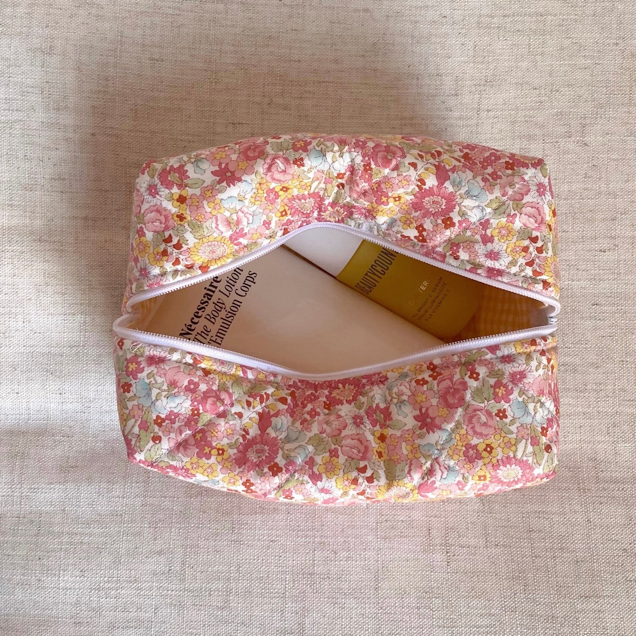 Floral makeup bag with open top and white zipper trim, interior products visible