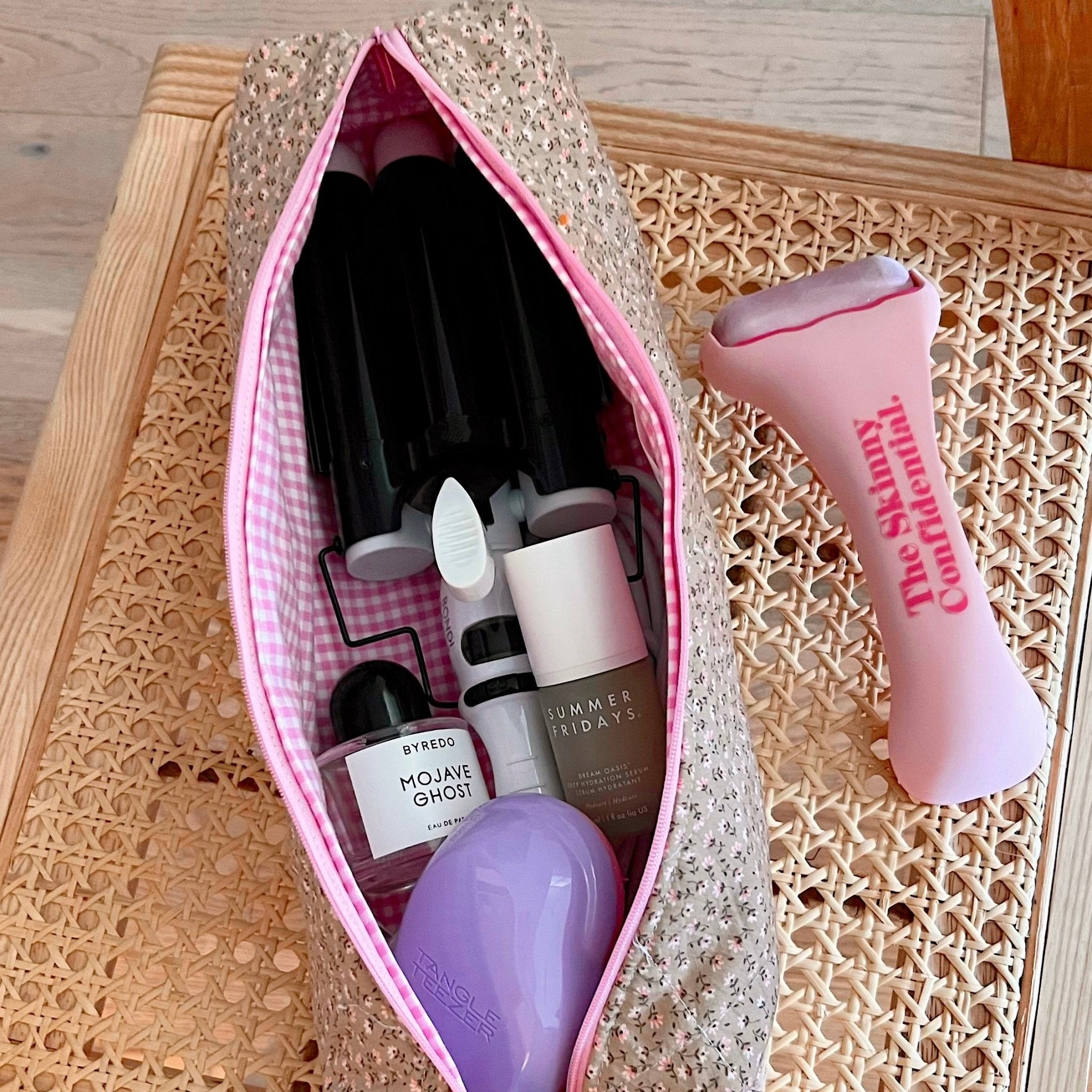 Tall tan floral toiletry bag with pink zipper and inner striped lining, bottles inside