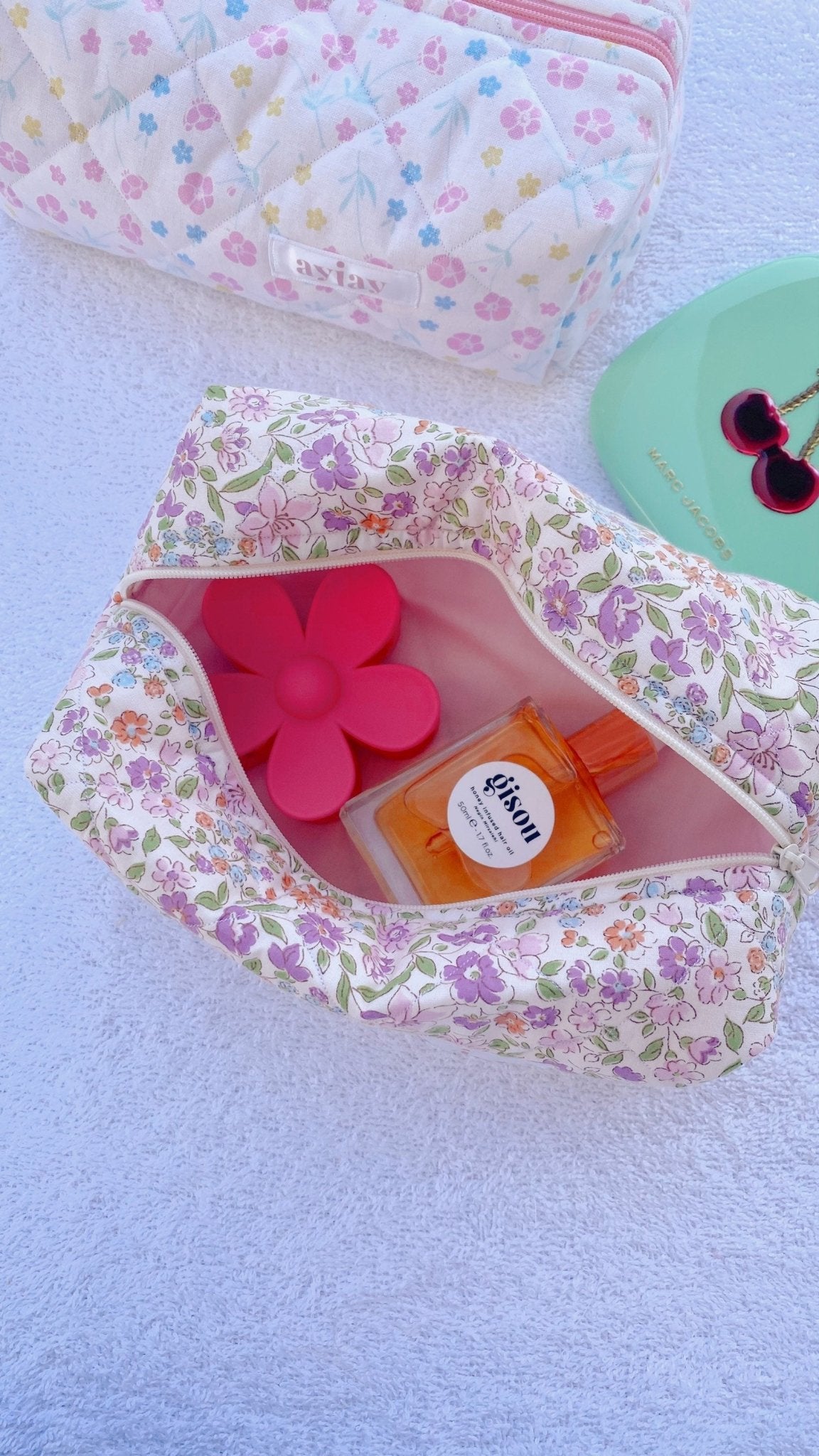 Purple floral zip pouch open with orange bottle and pink flower-shaped items inside