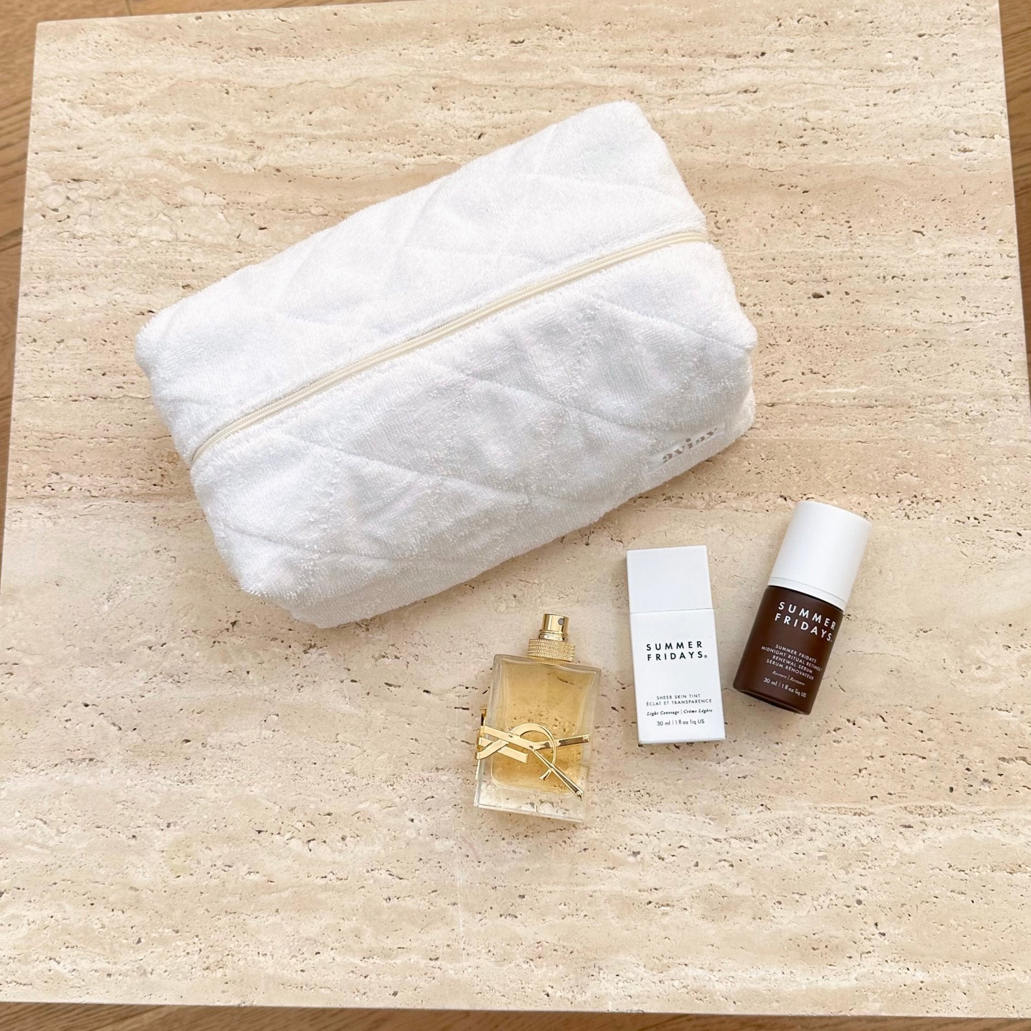 White terrycloth zip pouch, closed, with beauty bottles and cards beside it