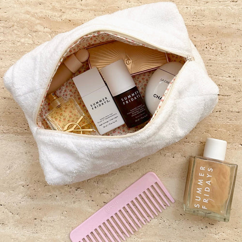 White terrycloth pouch with zip, ditzy floral lining and visible skincare items inside